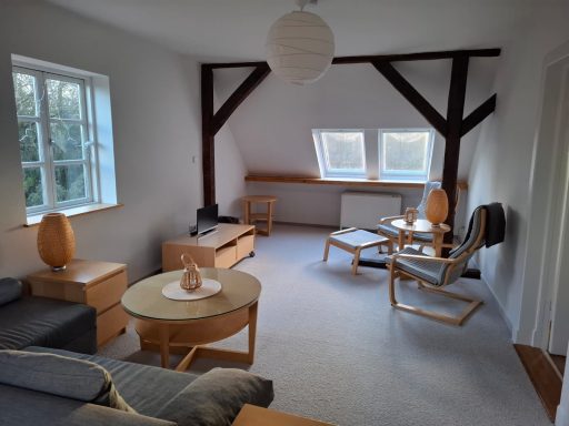 Heller Wohnraum mit Holzdetails, Sofa, Sesseln und einem runden Tisch.