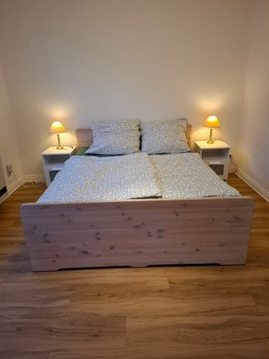 Doppelbett mit weißen Kissen, Nachttischen und Beleuchtung in einem hellen Raum.